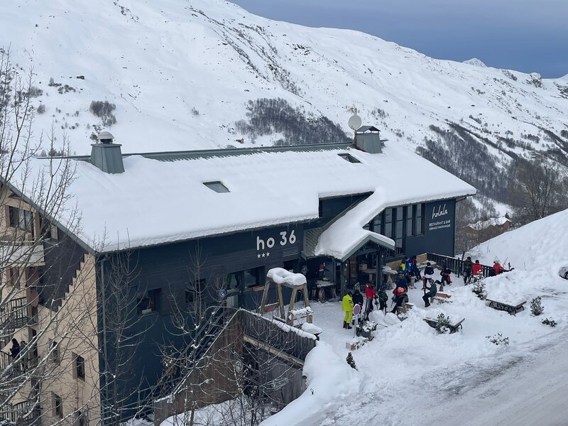 Snow-covered lodge with skiers gathering outside, nestled in a snowy mountain landscape.